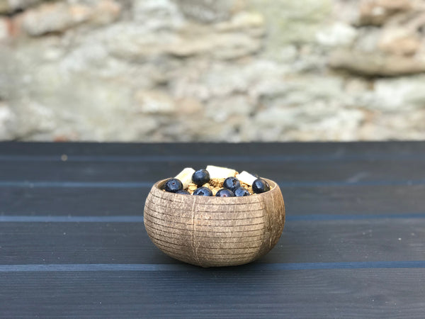 Blueberries, banana slices and granola in a coconut bowl, placed in front of a wall.