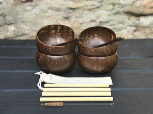 Four spoons inside four brown coconut bowls, four bamboo straws, a cleaning brush and a straw pouch on a wooden table.
